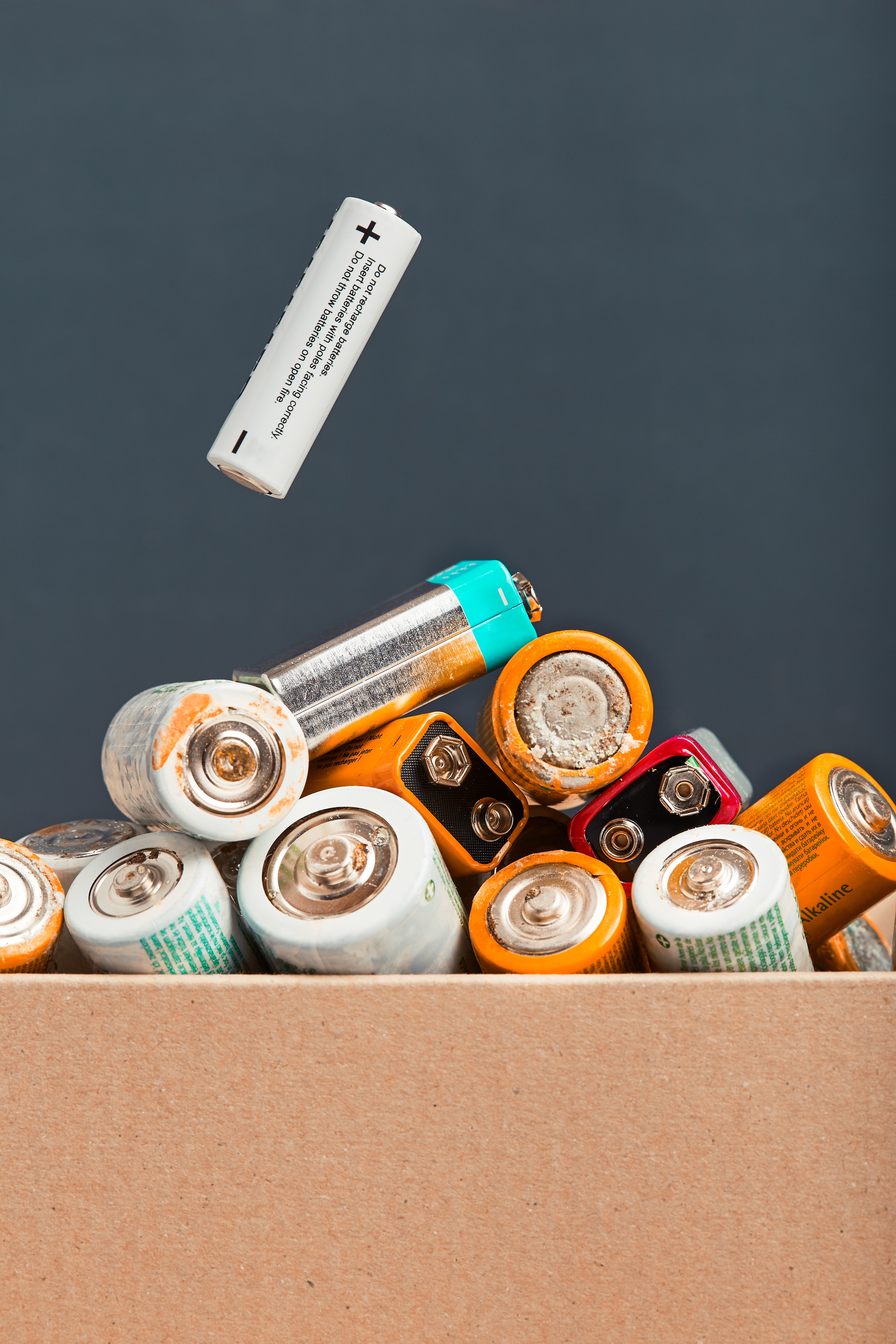 Used battery falling into a cardboard box filled with discharged